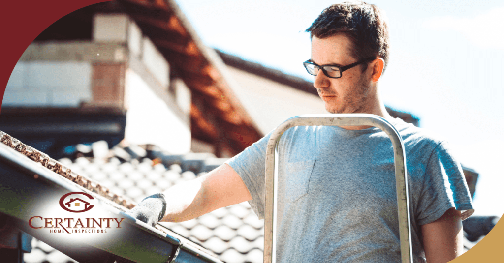 a person wearing glasses and a gray shirt, inspecting a gutter while standing on a ladder