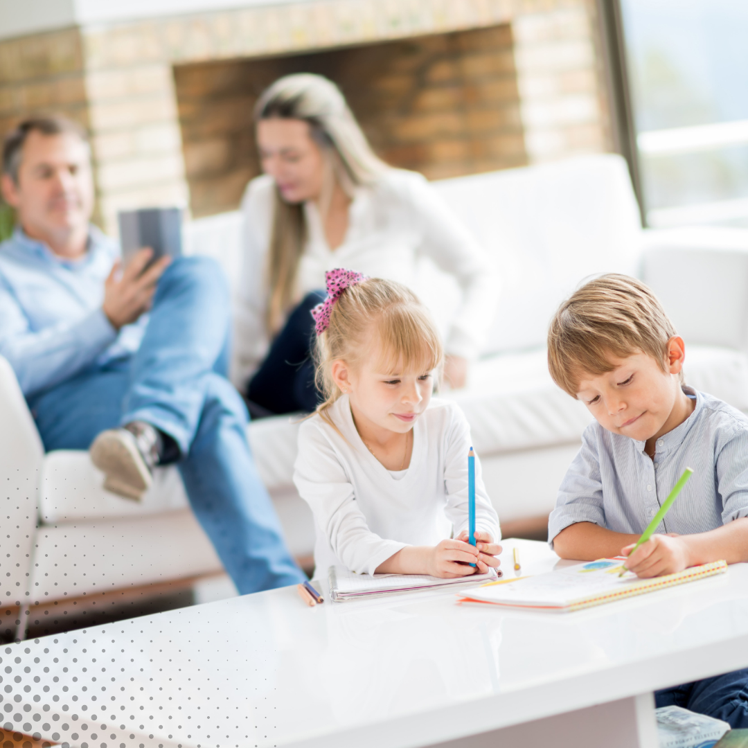 Two kids are busy with their homework at the table in a bright living room, as their parents unwind nearby.