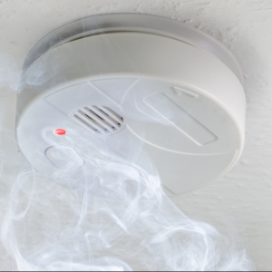 Smoke rising toward a ceiling-mounted smoke detector with an activated red light