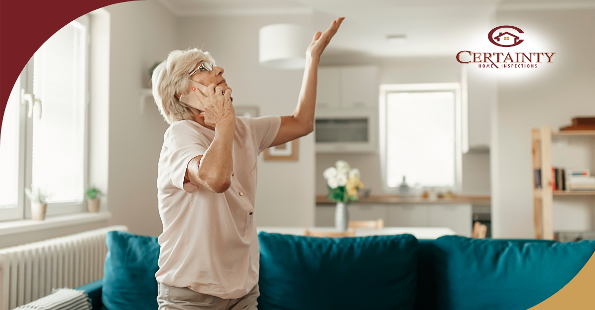 Woman on the phone looking up at a water leak in the ceiling.