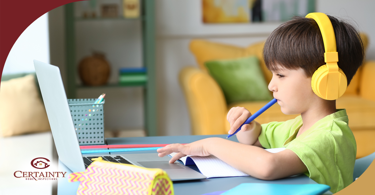 Young boy wearing yellow headphones studying on a laptop at home.